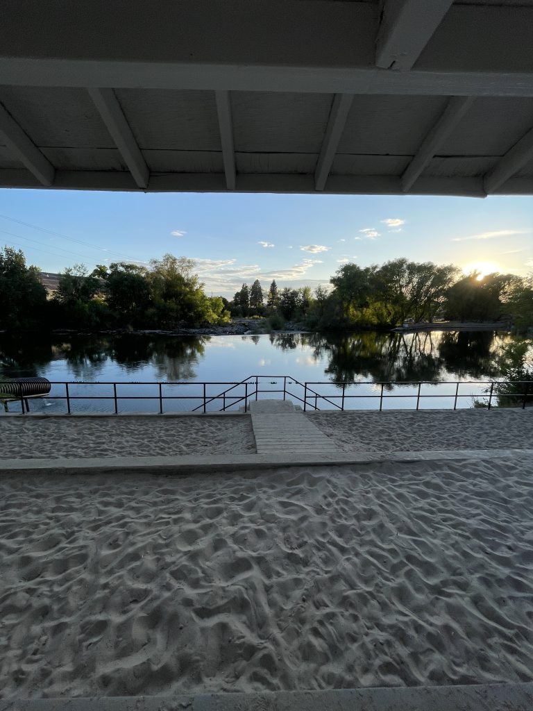 View of the sandbar at susnet from under the pavilion at the St. Anthony Sandbar with the river and tree line in the background.