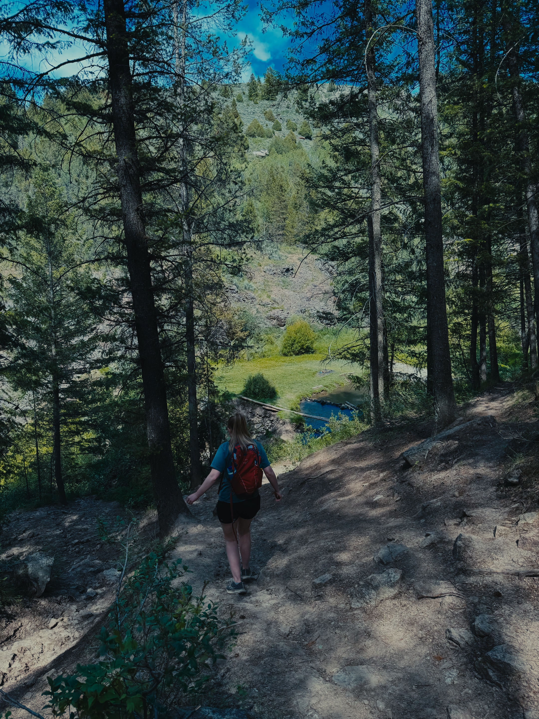 A hiker descending the dirt trail toward the Webster Dam pool and waterfall