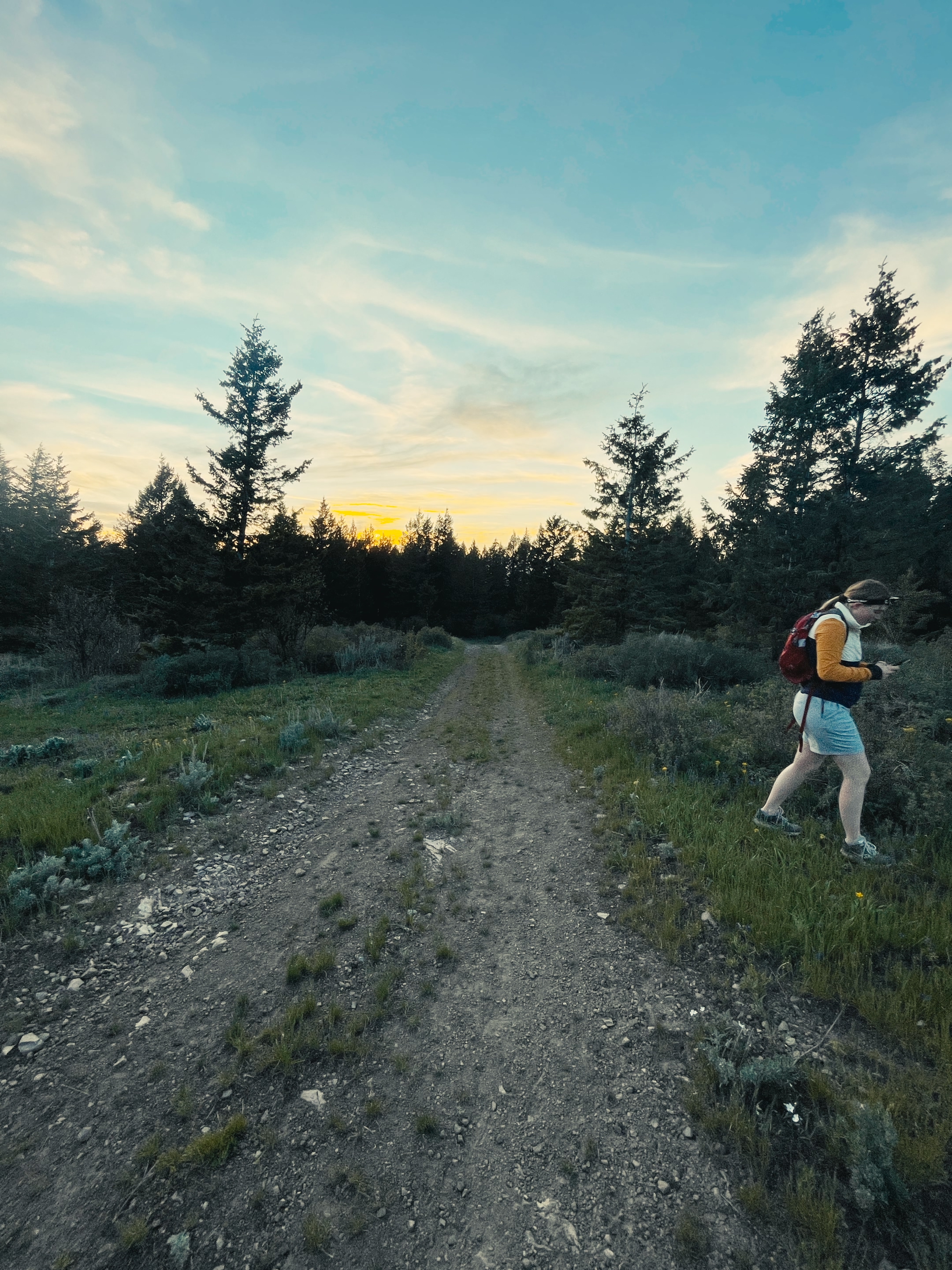 A hiker with a red backpack walking the Kelly Canyon Trail at dusk