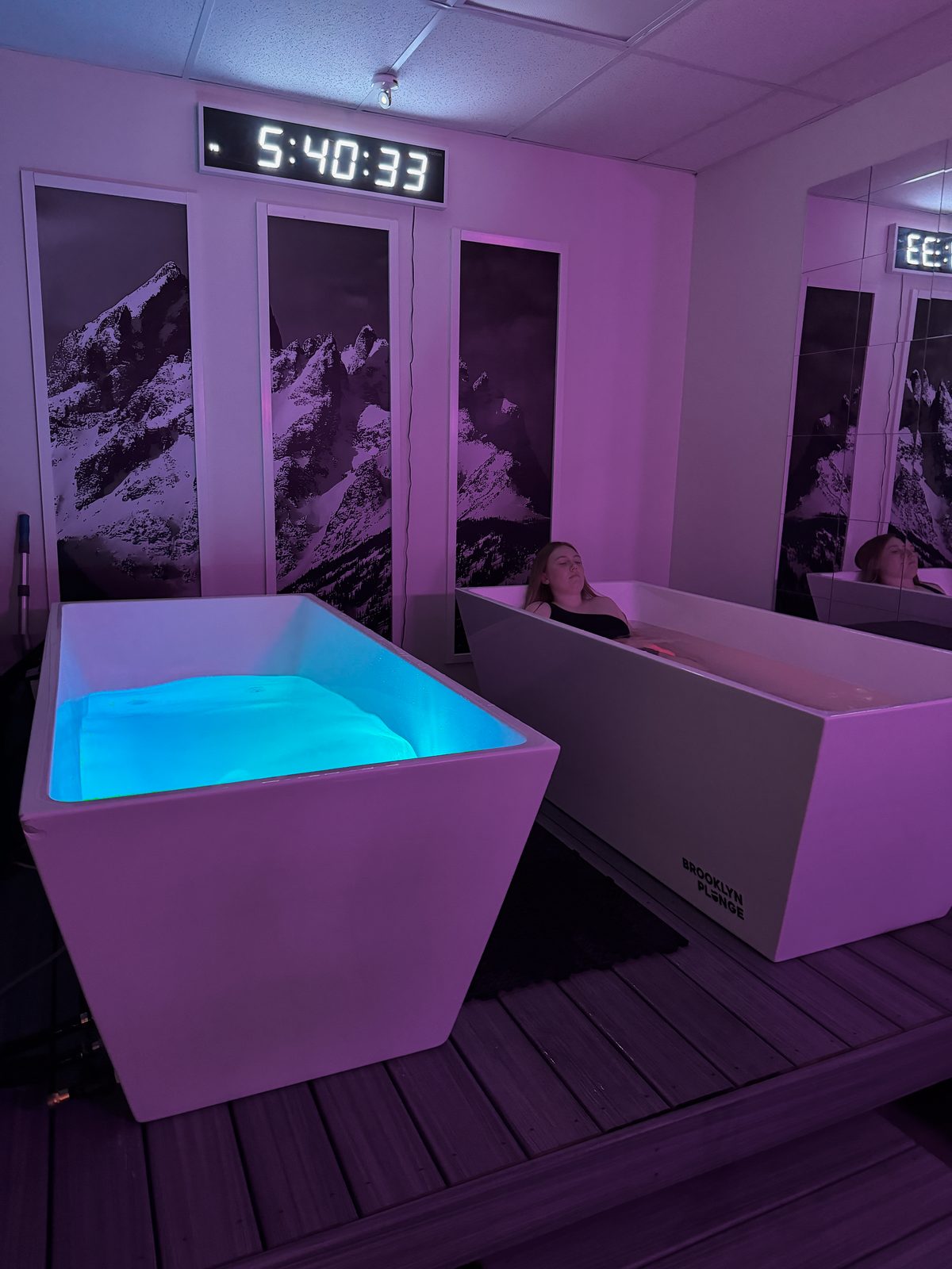 Two cold plunge tubs in a purple-lit recovery room at 8Peax Recovery, with a woman relaxing in one tub
